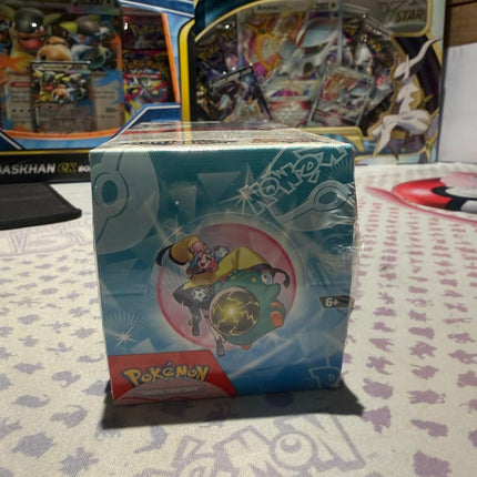 Pokémon trading card game booster pack on a table with other Pokémon products in the background.