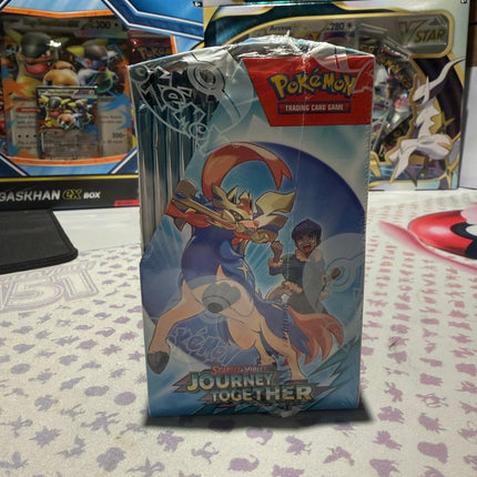 Pokémon trading card game pack on a patterned surface with other packs in the background